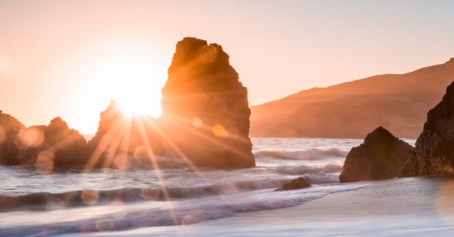 Sunrise appears through rock in the ocean