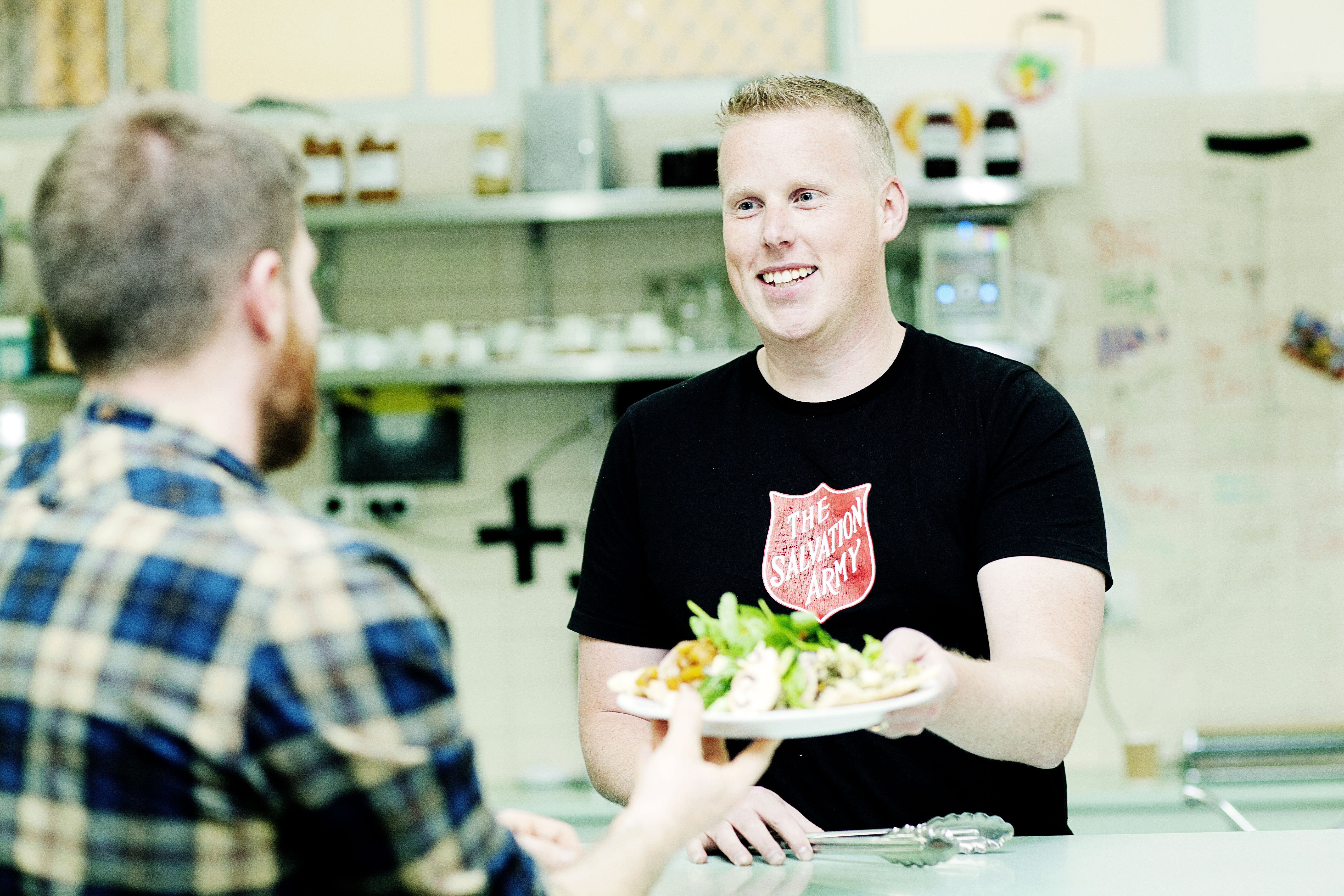 Salvation Army volunteer serving a plate of food to a bearded man